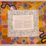 Colourful Aboriginal painting with the Uluru Statement in the middle. The statement is surrounded by signatures.